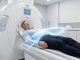 Illustration médicale réaliste d’un homme allongé sur la table d’un scanner dans un hôpital moderne, avec un faisceau de rayons X bleu-blanc représenté de manière sobre autour de son torse.